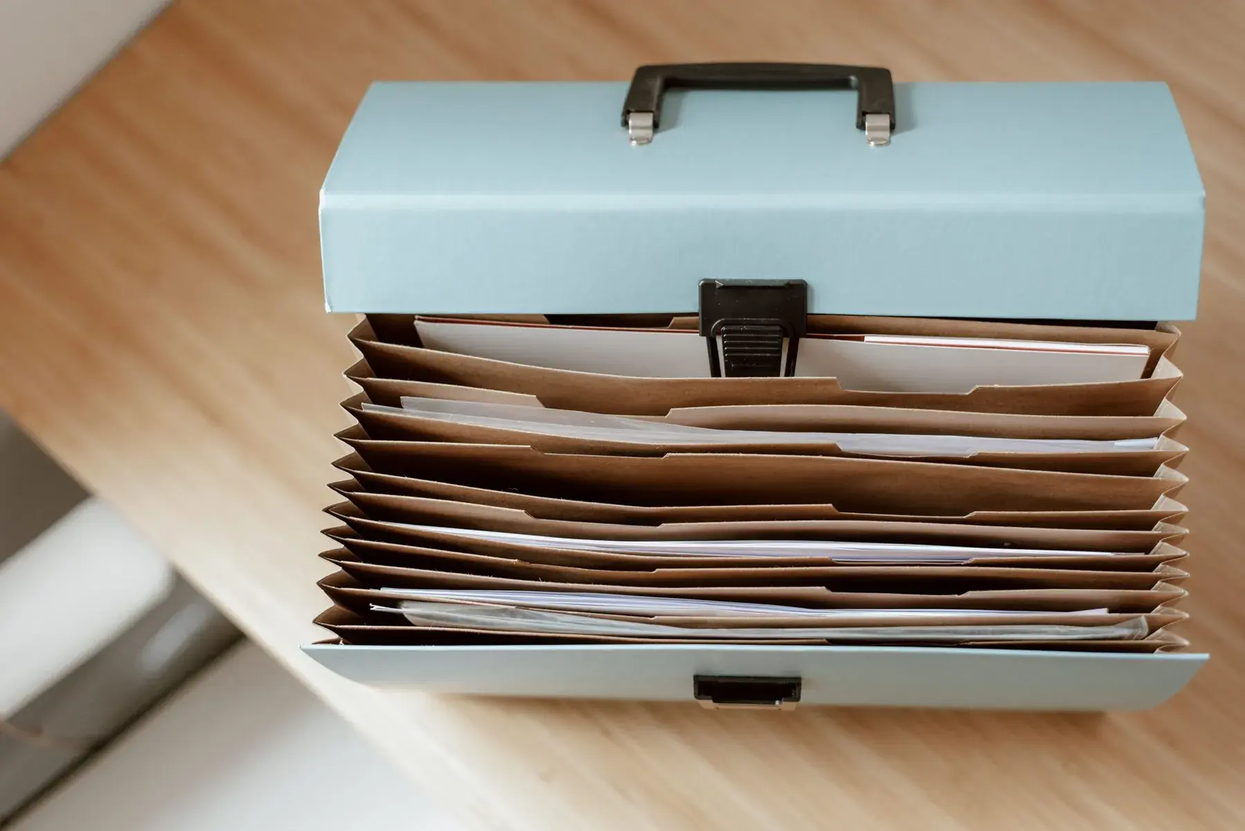 A blue file box full of folders on a wooden table.