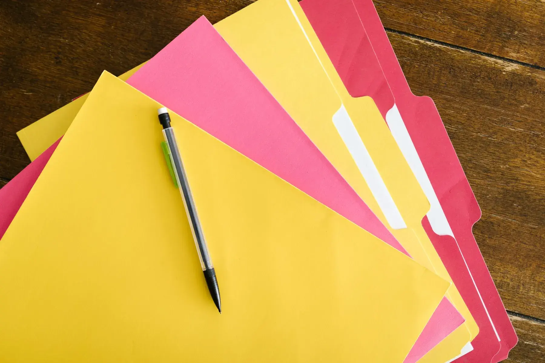 Yellow and pink folders and a pen on a wooden table.