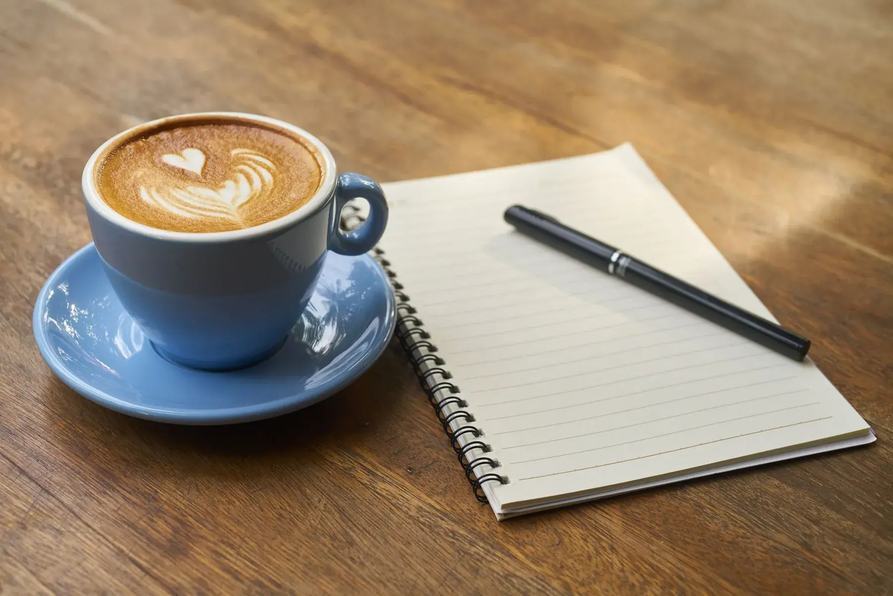 A coffee in a blue cup next to an open notebook.