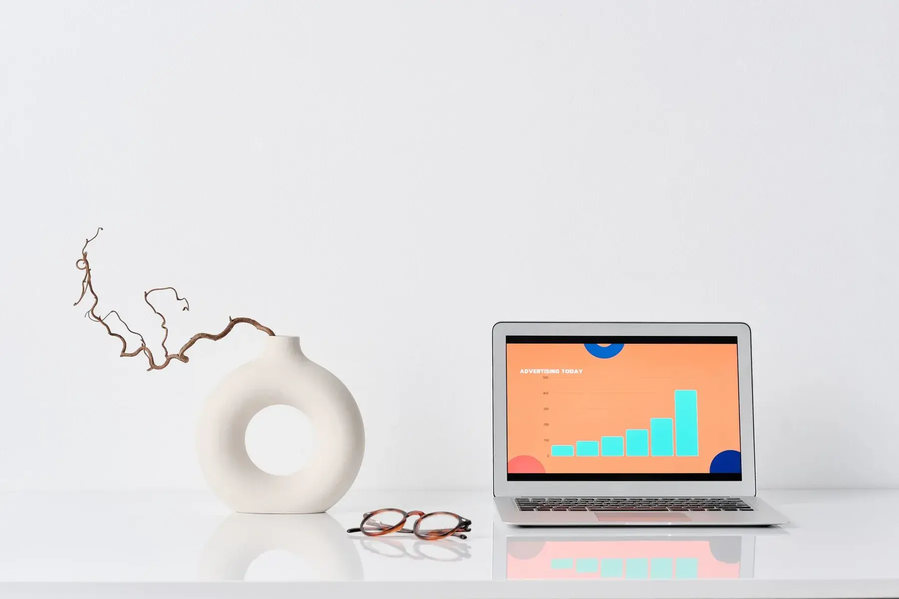 A laptop showing a chart, next to a vase and glasses.