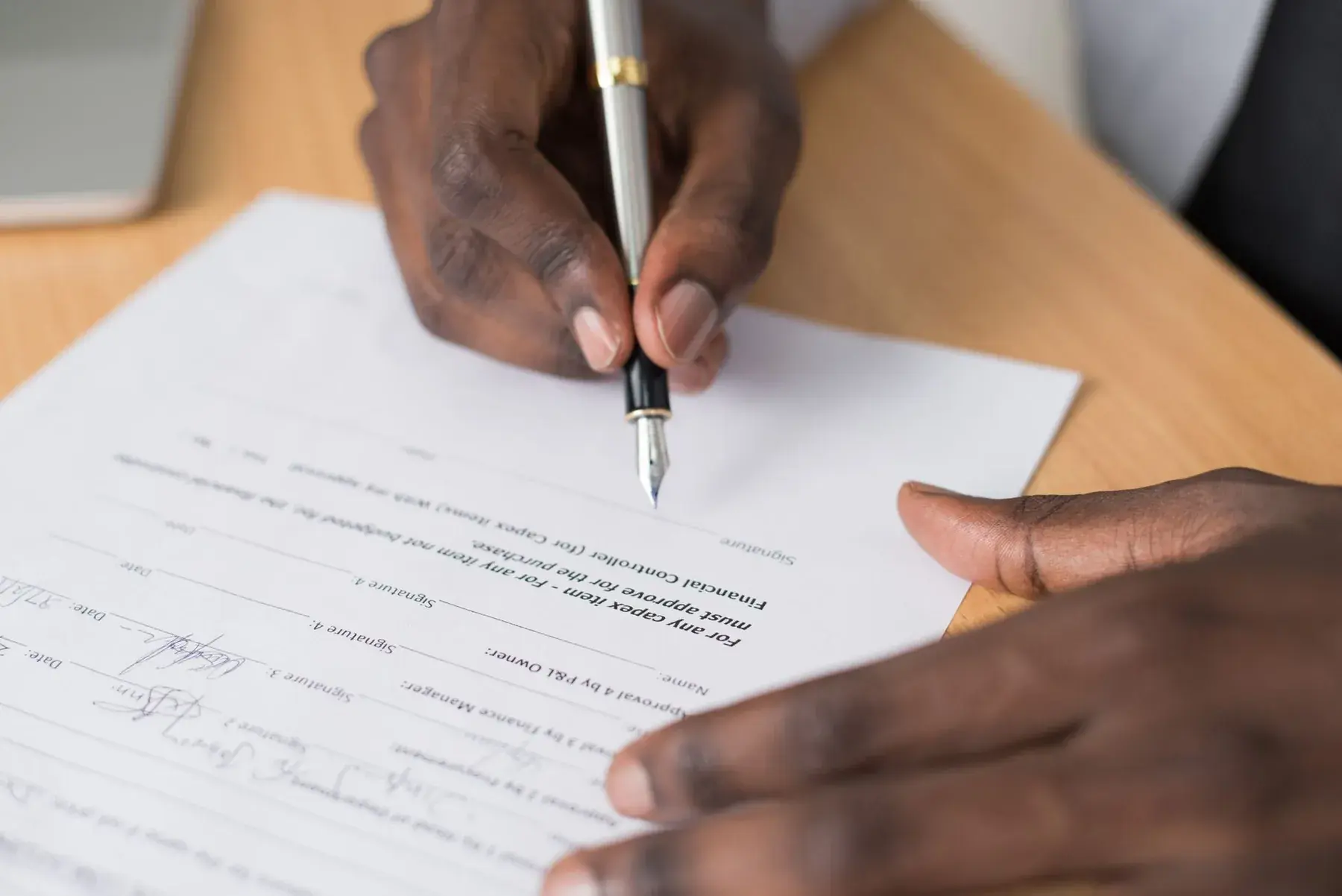 Two hands and a pen over a contract to sign.
